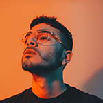 Young man with glasses looking upward against an orange background.